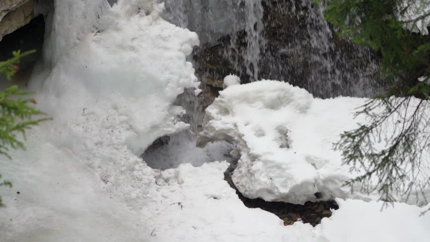 Waterfall in winter with ice formations and light snowfall at Johnston Canyon.