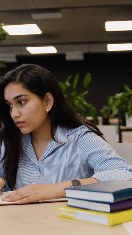 Young Indian student woman writing and studying with laptop in library