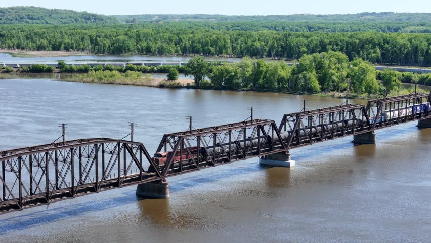 Aerial 4K video of a Railroad locomotive pulling a freight train across the Mississippi river on a trestle bridge
