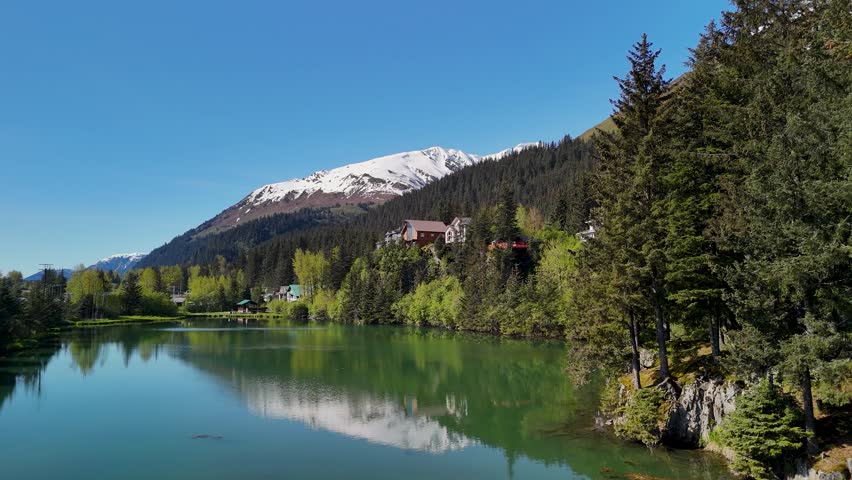Seward, Alaska downtown sits near the shoreline bay area under a clear blue sky in summer. Boats, buildings, and mountains create a scenic coastal view. Perfect stock footage for travel, tourism, cityscape, and Alaskan summer landscape projects.