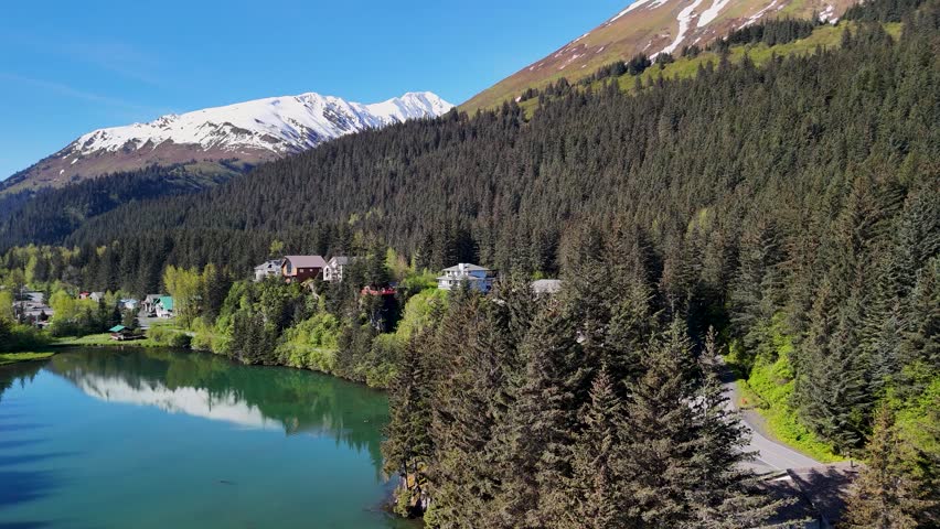 Seward, Alaska downtown sits near the shoreline bay area under a clear blue sky in summer. Boats, buildings, and mountains create a scenic coastal view. Perfect stock footage for travel, tourism, cityscape, and Alaskan summer landscape projects.