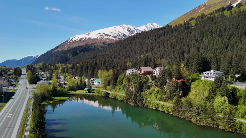Seward, Alaska downtown sits near the shoreline bay area under a clear blue sky in summer. Boats, buildings, and mountains create a scenic coastal view. Perfect stock footage for travel, tourism, cityscape, and Alaskan summer landscape projects.