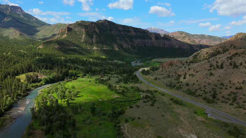 Aerial Montana USA landscape reveals dramatic red rock cliffs towering above winding highway and river valley.