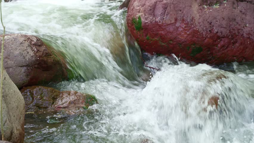 Close up of fast mountain river stream flowing between large rocks, with rushing clear water in natural outdoor landscape.