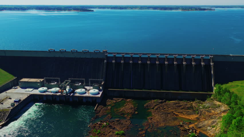 Hartwell Dam showing 13 spillway gates, hydroelectric powerhouse with turbine units, exposed rocky riverbed below, and Lake Hartwell reservoir on the Georgia–South Carolina border.