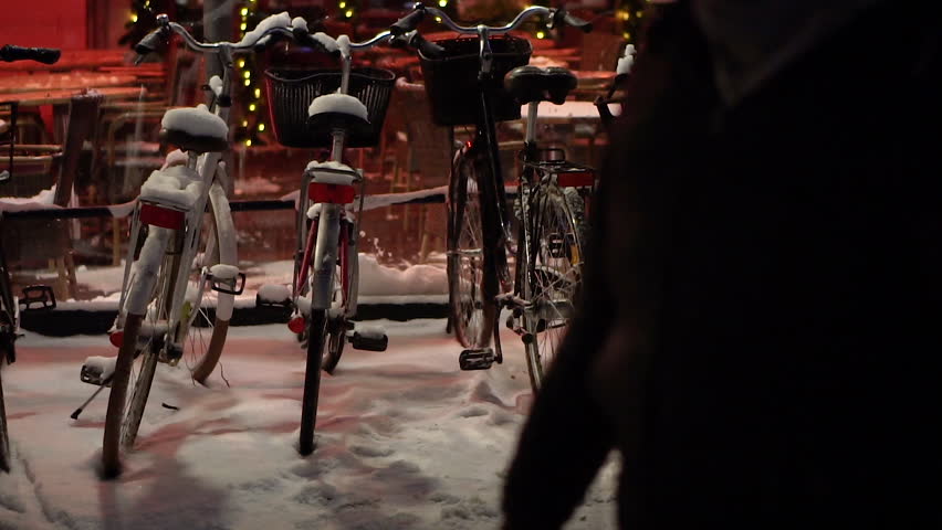 Bicycles parked on snowy street near cafe in evening atmosphere.