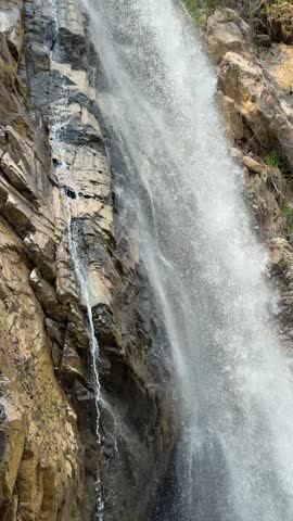 Vertical view shows a waterfall stream flowing down a steep rock surface forming a vertical cascade composition inside a rugged canyon. Natural beauty.