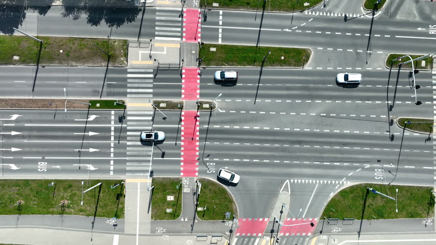 Cinematic aerial topdown shot of a modern urban road intersection featuring red bicycle paths, pedestrian crossings, and light traffic in Gdynia, Poland.