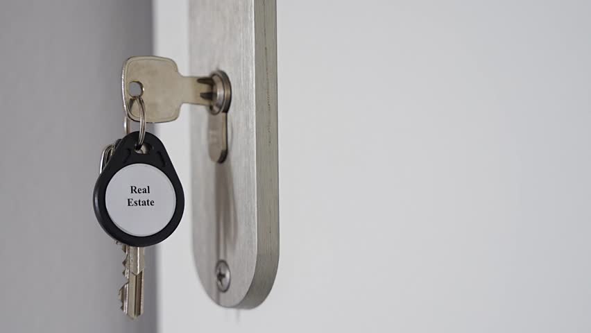House keys with Real Estate keychain inserted into apartment door lock with copy space. Property ownership and housing market concept for real estate business and home purchase.