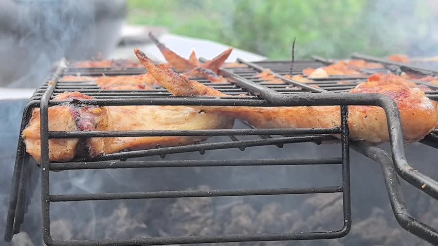 Juicy chicken wings sizzle over an open flame, enveloped in fragrant smoke. The sun casts warm light as the cook expertly flips and seasons for delicious flavors.