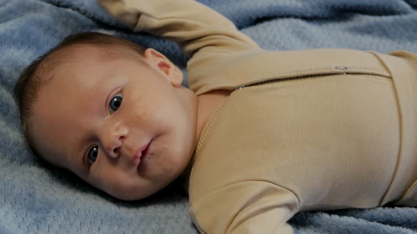 Adorable newborn baby with big blue eyes lying on a soft blue blanket making funny faces