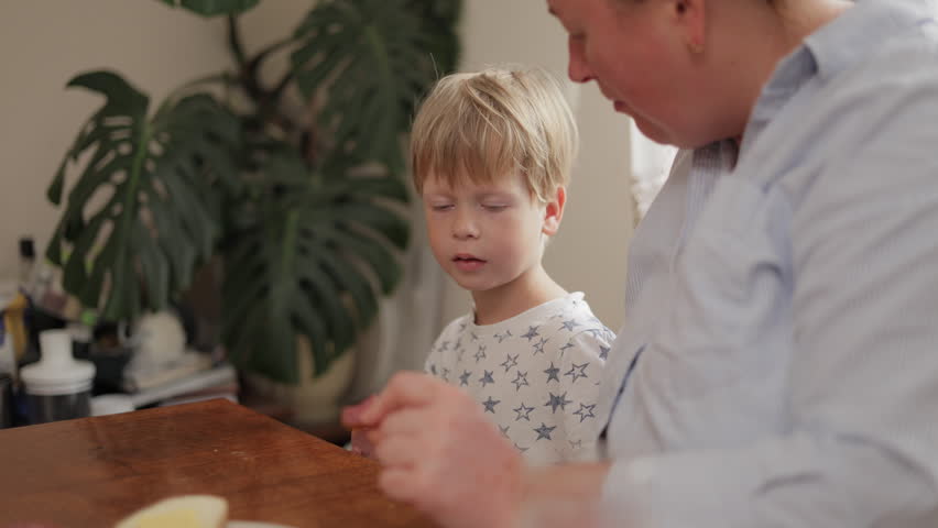 Young boy in pajamas having a meal with his mother in the kitchen during the morning