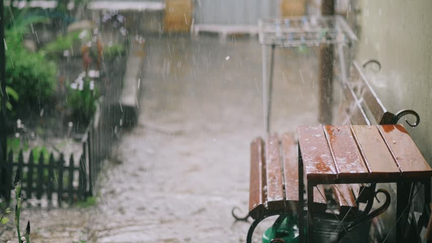 Strong rainstorm with hail falling in residential backyard near wooden bench during bad weather outdoors