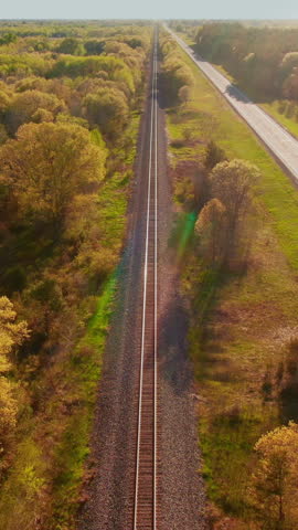 A railway line running parallel to a highway amidst lush greenery in Wisconsin. Captures the contrast between nature and infrastructure. Suitable for transportation or landscape vertical posts
