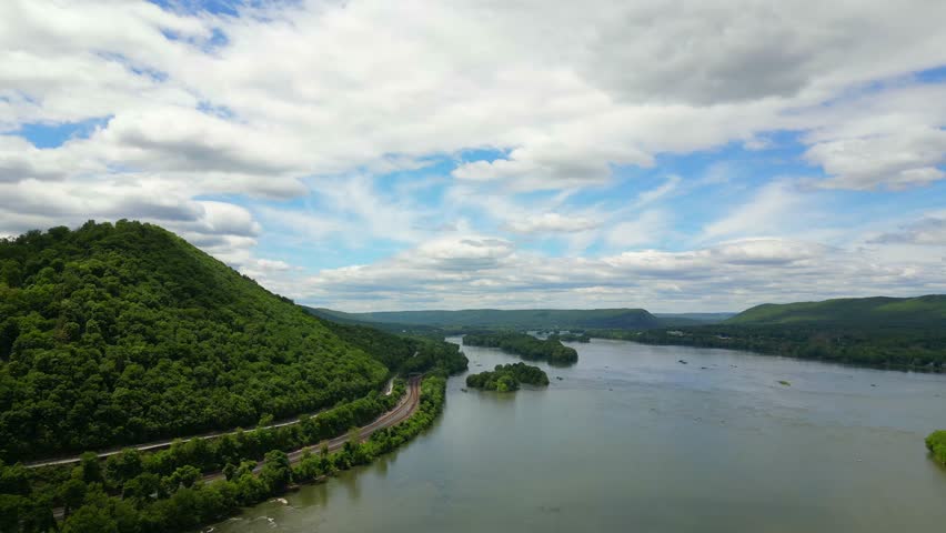High-altitude drone footage capturing a wide, sweeping view of a large river splitting lush green forested hills and mountain ridges.