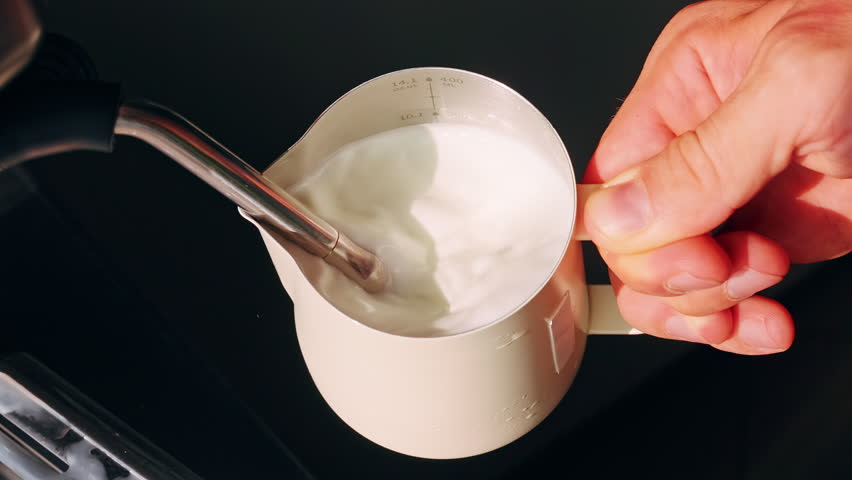 Top Down View Of Hand Holding Milk Pitcher While Steam Wand Froths Milk Creating Smooth Texture In Slow Motion, Latte Preparation.