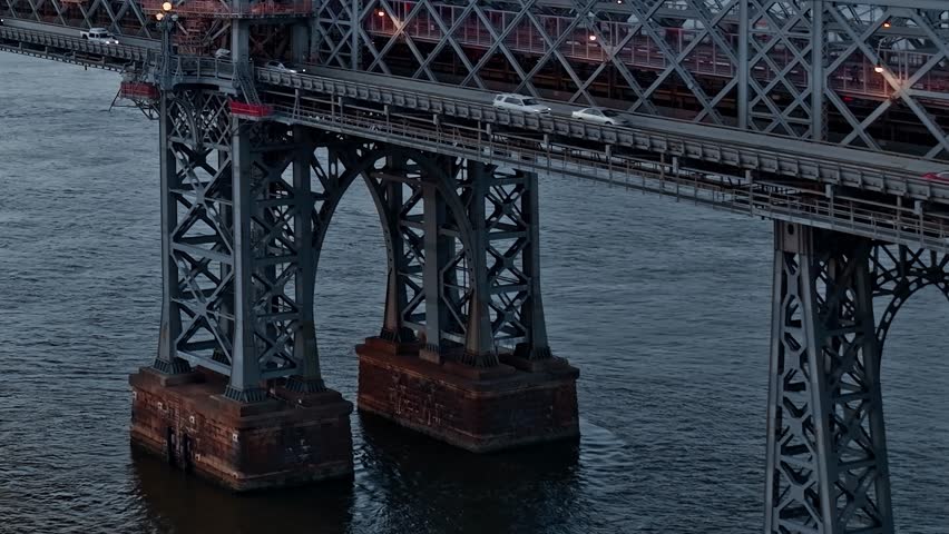 Close-up drone shot of the Williamsburg Bridge support towers and lower roadway with cars during twilight in New York City.