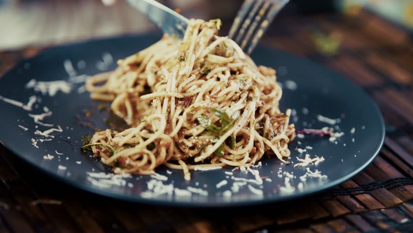 Pasta with Cheese. Hands Using Knife and Fork for Eating Fresh Italian Spaghetti in Dark Plate. Dinner Meal Prep Process and Gourmet Kitchen Development. Homemade Food Recipe Components. Traditional Mediterranean Dish Cooking. Domestic Culinary Lifestyle. Pasta with Cheese Routine. Hot Bolognese Meat Sauce and Grated Ingredient Decoration. Restaurant Table Serving. Pasta with Cheese