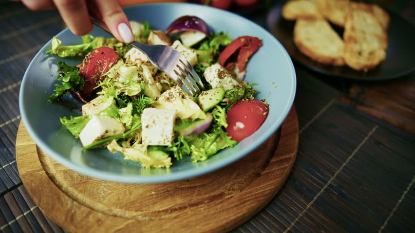 Salad with Cheese. Female Hand Mixing Fresh Greek Appetizer in Blue Bowl. Caucasian Woman Eating Organic Vegetable Recipe. Sliced Feta Cubes and Red Tomatoes. Homemade Lunch Prep Process and Gourmet Kitchen Development. Domestic Culinary Lifestyle. Salad with Cheese Routine. Traditional Mediterranean Dinner Dish. Restaurant Menu Meal Preparation. Salad with Cheese