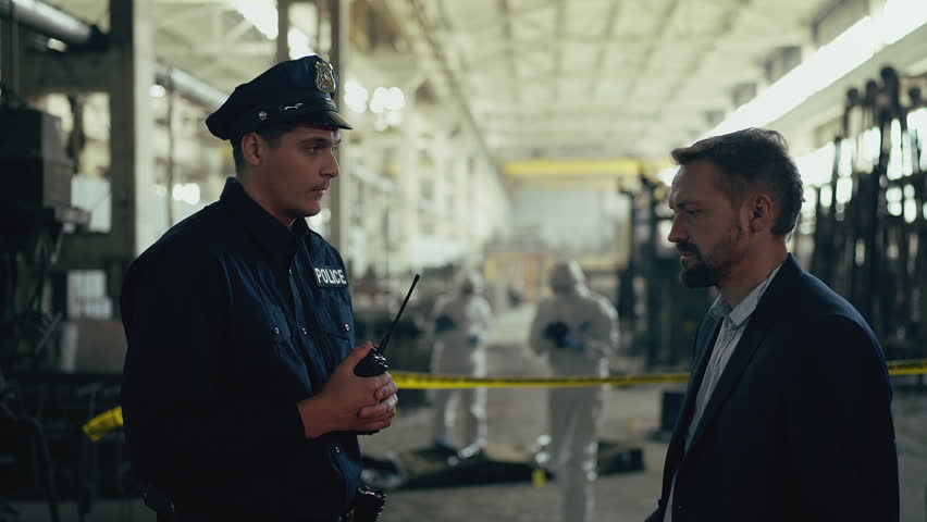 Police officer speaking with detective about investigation at metal factory