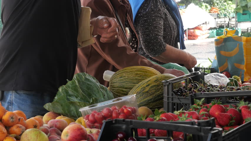 Busy Farmers Market Stall With Fresh Fruit, Vegetables and Customers. Crowded farmers market scene with customers choosing fresh fruit and vegetables at an outdoor stall, showcasing colorful strawberries, melons, peaches and leafy greens in a lively community setting.