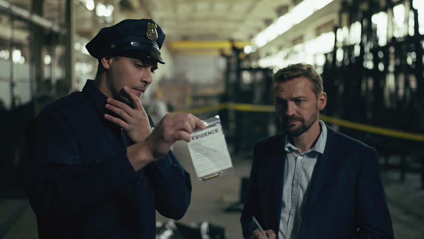 Police officer and detective discussing evidence at industrial crime scene