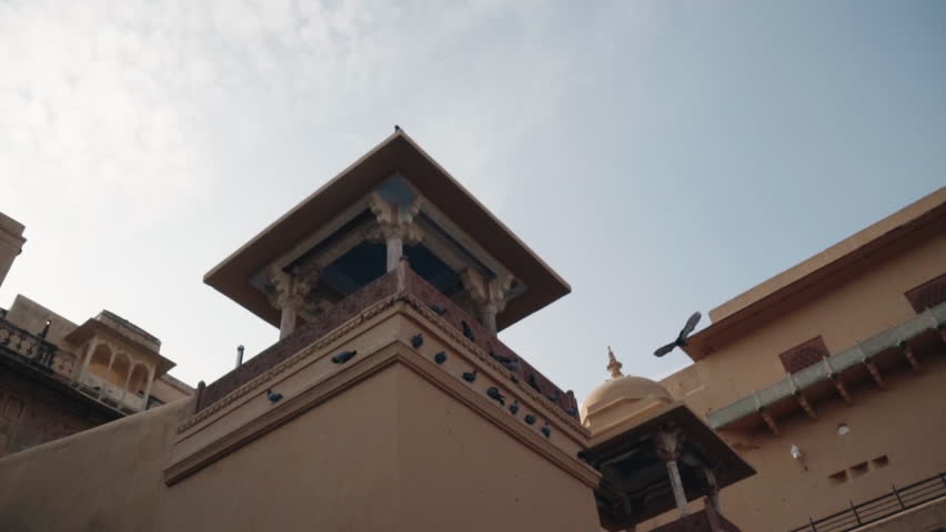 Low angle view of pigeons perching and flying around a majestic sandstone tower of a historic Indian fortress, revealing the intricate details of ancient Mughal and Rajput architecture