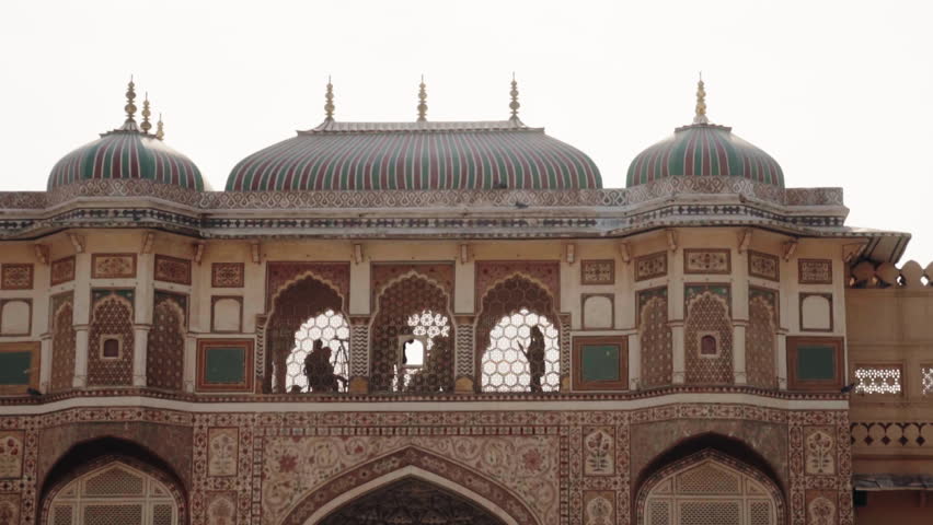 Intricate architecture of the famous Patrika Gate in Jaipur, India, with silhouetted figures of people visible through the ornate arched windows against a bright sky, showcasing a popular landmark