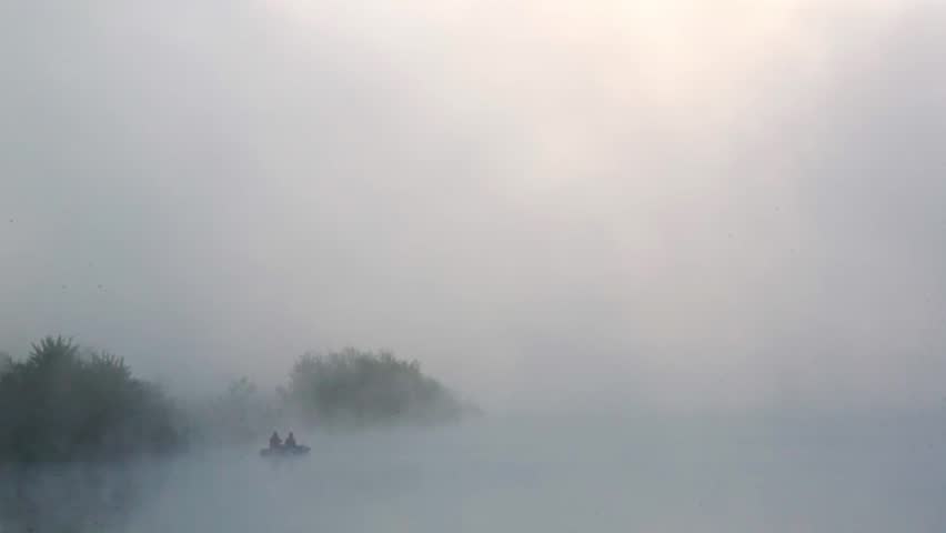 Two people in a boat in a lake, fishing at sunrise, with fast-moving vapor and clouds