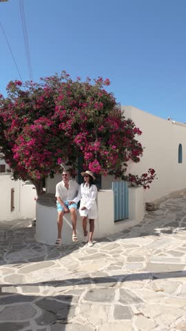 A diverse couple explores the vibrant streets of Lefkes Paros, Greece, under a bright blue sky. A couple enjoys a leisurely moment by a blooming bougainvillea, soaking in the islands beauty and charm.