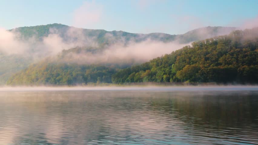 View of a lake in the morning with clouds passing through hills