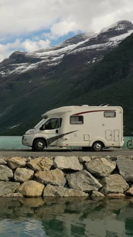 Motorhome parked by mountain lake in dramatic alpine landscape, vertical travel scene.
