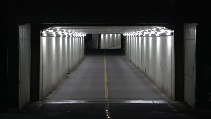 Front view of a small, narrow two-lane road tunnel in Seoul at night with bright white lights inside and darkness outside, creating a mysterious liminal space atmosphere.