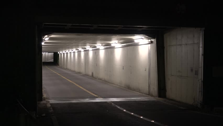 Diagonal side angle view of a small, narrow two-lane road tunnel in Seoul at night, showing a deep perspective with bright interior illumination.
