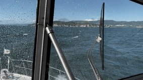 Point of view from a small boat cockpit with raindrops on the windshield, crossing choppy sea toward a rugged volcanic coastline in Kamchatka, Russia on a clear day - Powered by Shutterstock - Get 15% off with code: PIKWIZARD15