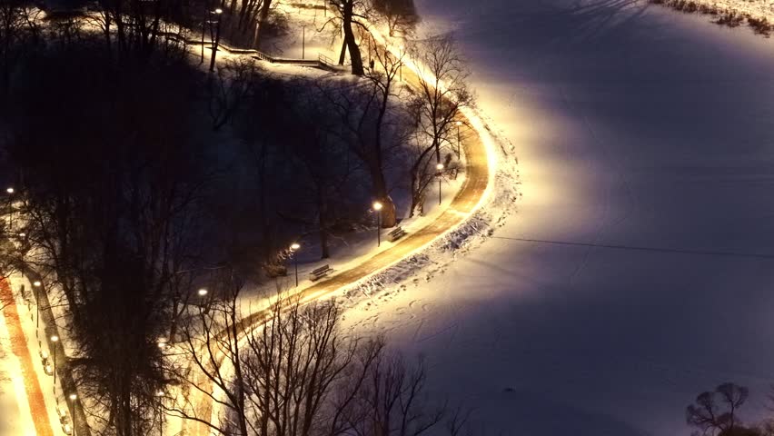 Wlking path illuminated by streetlights in a city park in aerial view on winter evening