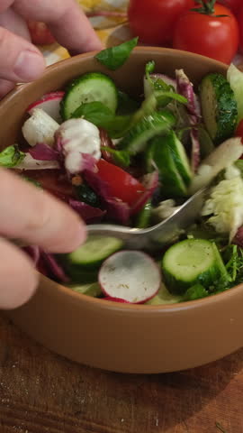 Vertical video. Woman cooking vegetable salad. Preparing diet summer food. Hands using spoon to mix salad ingredients in plate. 