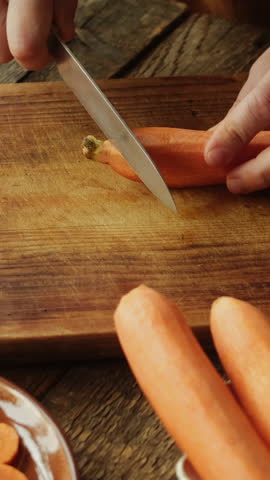 Vertical video. Hands slicing carrot with a knife. Healthy vegetarian food, raw food diet.