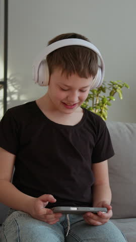 Young boy wearing headphones plays mobile game on couch, showing excitement and joy