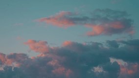 Wide static upward view of soft pastel clouds drifting across an open teal-blue sky during early dawn or sunset. The frame has a minimal atmospheric composition with scattered cumulus clouds illuminated by gentle pink and peach light. A small bird occasionally appears high in the sky, adding subtle natural movement to the calm scene. - Powered by Shutterstock - Get 15% off with code: PIKWIZARD15
