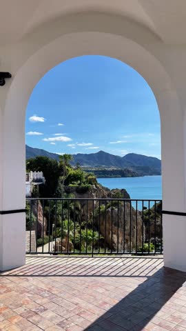 Scenic view of the Mediterranean sea and mountains through a white arch at Balcon de Europa in Nerja, Andalusia, Spain, beautiful coastal landscape and traditional Spanish architecture on a sunny day.