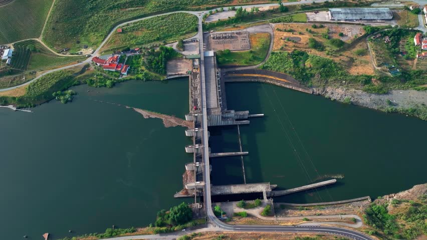 Overview of a hydroelectric power plant with dam infrastructure located by a river. Water flows through turbines to generate electricity continuously.