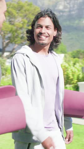 Vertical video: Heading to yoga class long-haired man in hoodie holding purple mat on lawn. Outdoor, fitness, group, friends, mountains, poolside, vertical video
