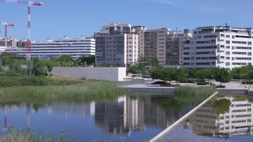 Modern residential apartment buildings reflected in calm water of urban park pond. Contemporary city architecture with landscaped public space and peaceful atmosphere