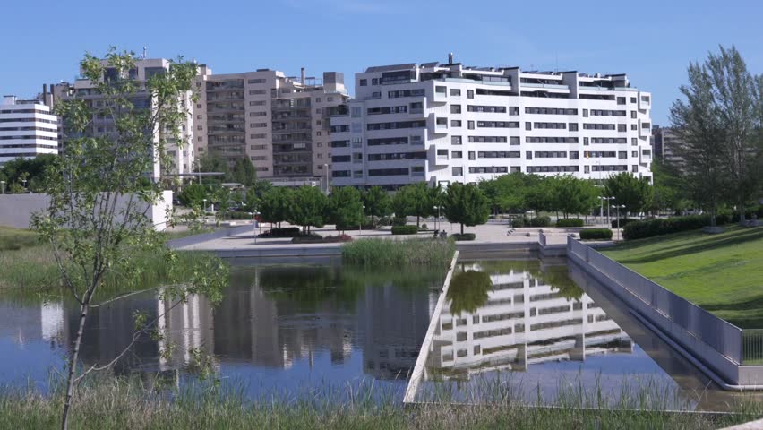 Modern residential apartment buildings reflected in calm water of landscaped urban park pond on sunny day. Contemporary city architecture and peaceful urban environment
