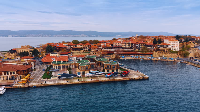 Approaching the sea shore with multiple low-rise houses. Colorful cityscape of Nessebar, Bulgaria on gloomy day.