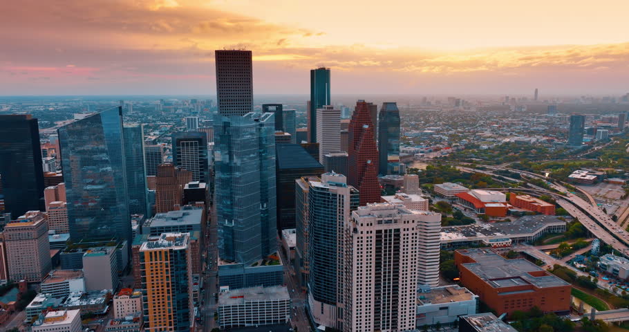 Approaching the high-rises in the downtown Houston, Texas, USA at sunset. Numerous cars move by the highways around the city center. Orange cloudy sky at backdrop.