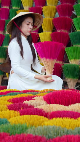 Vertical video Asian woman wears traditional white Vietnamese cultural clothes with a conical hat and colorful incense sticks.