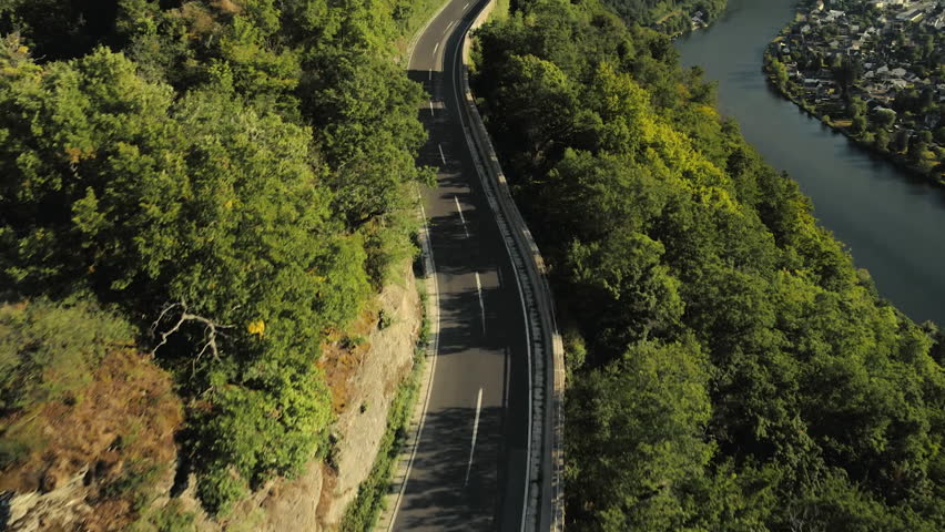 Stunning aerial view of a road through a green forest, following a wide river with a town on its banks
