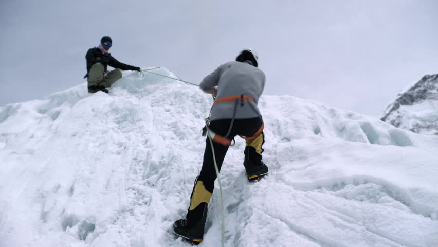 Two mountaineers roped together ascending a steep, icy wall in a snowy mountain range